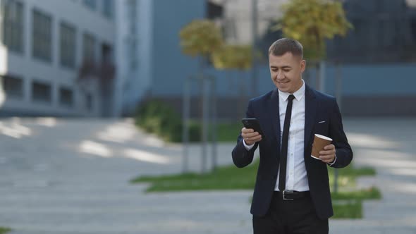 Stylish Businessman Exiting from the Modern Office Using his Smartphone Sliding on Mobiles Screen