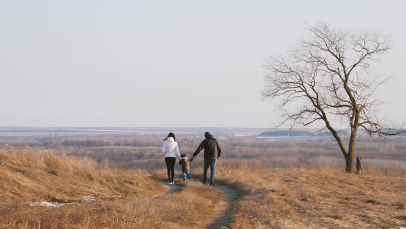 Happy Family Walking in the Meadow Near a Big Tree During Sunset