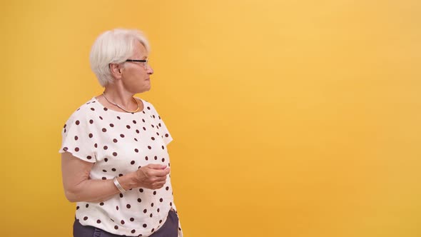 Senior Woman Pointing Finger on Empty Advertisement Space, Orange Background