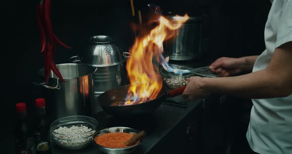 Close-up of a Chef Preparing a Dish in a Frying Pan. Oil and Alcohol Ignite with an Open Flame in