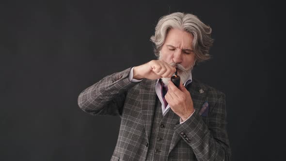 Mature Man Smoking Pipe and Looking at It Isolated on Black Background.