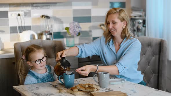 Mom Pouring Tea Into Cups When Sitting at Kitchen with Child Daughter Rbbro