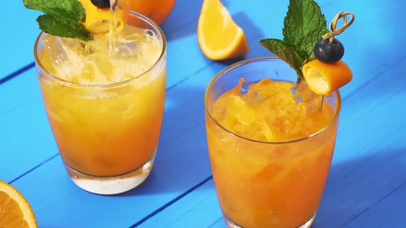 Soda water being poured into glasses of an orange cocktail drinks on blue wooden table