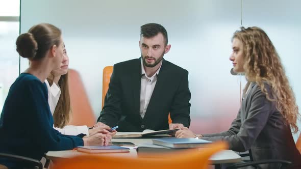 Serious Unsatisfied Caucasian Man Scolding Women Sitting at Table in Office Indoors