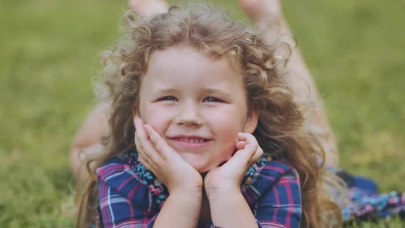 A Little Curlyhaired Girl Lies on the Grass in the Garden