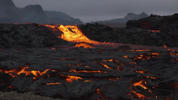 Stream of incandescent lava flowing in desolated landscape