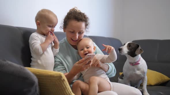 Young Mother Plays Games on Phone with Two Girl Twins and Curious Pet on Sofa