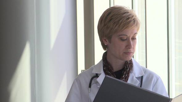 Woman Doctor Looks At Patients Chart Then Looks A The Camera With A Worried Look