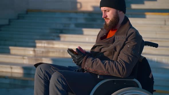 Wheelchairbound Man is Chatting By Smartphone Outdoors in City