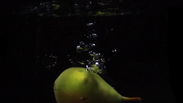 One Pear Falls Into the Water with Splashes and Bubbles in Slow Motion.