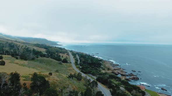 Aerial footage of a road, a rocky ocean coast, waves, trees, fog at Garrapata, California, USA