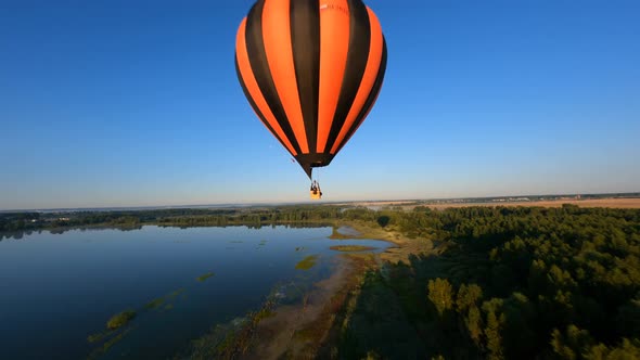 drone manoeuvres up and down around Black and orange hot air balloons above lake