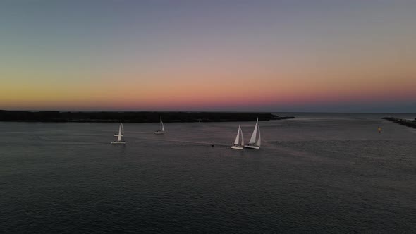 High panning panoramic view of a group of fasting sailing boats against a colorful sunset backdrop