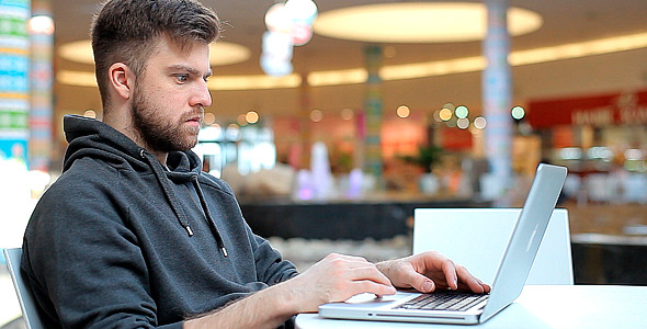 Man Working at a Laptop in a Shopping Center