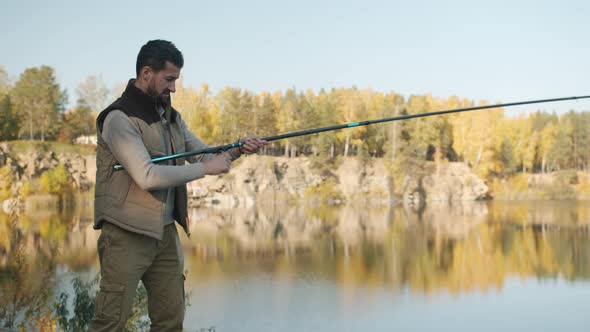 Young Fisherman in Casual Clothing Catching Fish with Rod Against Natural Background