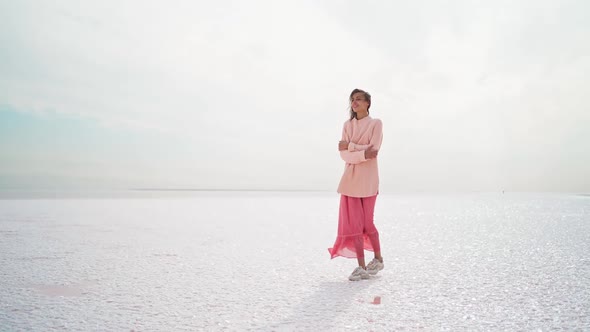 Wonderful Dreamy Woman in Big Sweater and Pink Dress Posing at Windy Salty Coastline on Pink Salt