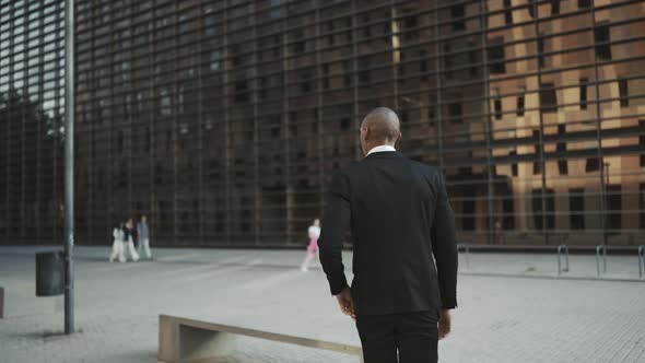 Back view of African businessman walking and sitting on the bench while typing by phone