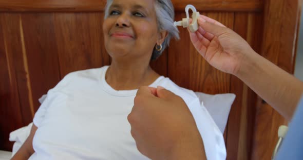 Female doctor inserting hearing aid in senior black woman ear in a comfortable home 4k