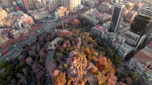 Aerial orbit of Santa Lucia Hill with autumnal trees, traffic in Alameda avenue, Santiago city build