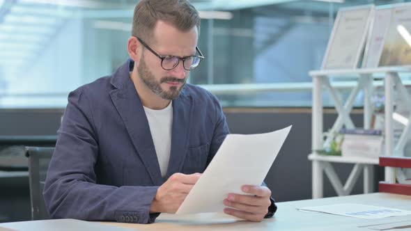 Middle Aged Businessman Upset While Reading Documents in Office