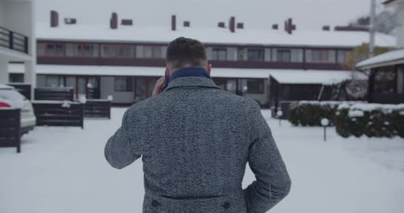 A Man Walks Down A Snowy Street And Talks On The Phone. View From The Back