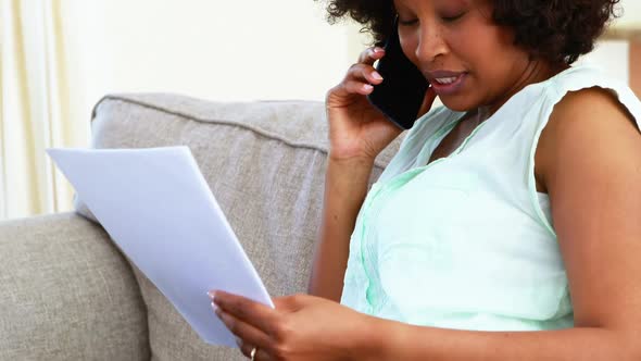 Woman talking on mobile while looking at documents in living room