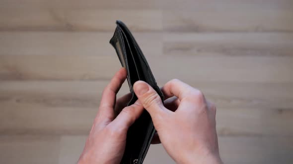 Person Opens Empty Black Wallet and Throws on Brown Laminate