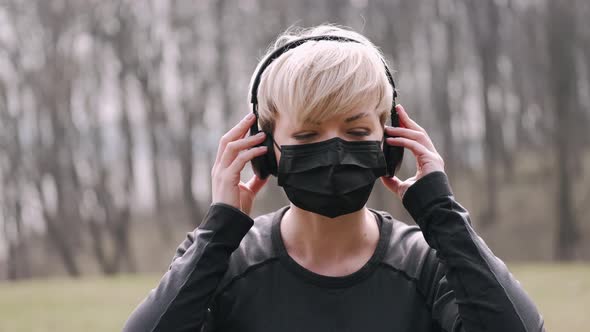 Athletic Woman in a Mask Is Listening To Music in Earphones