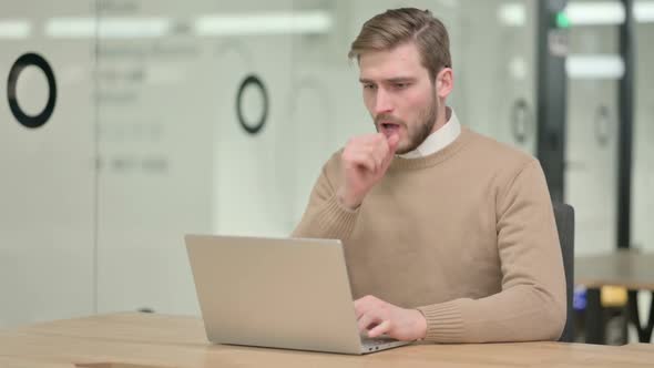 Creative Young Man with Laptop Coughing in Office