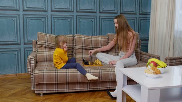 Small Cute Daughter Child and Young Mother Playing Chess at Home Sofa Leisure Hobbies Activities