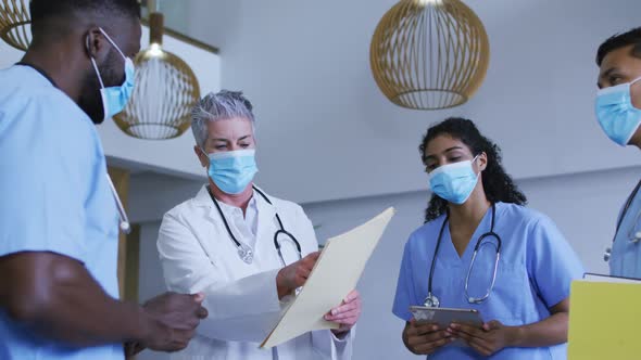 Diverse group of male and female doctors in face masks looking at files and discussing in hospital