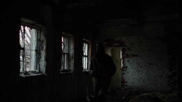Silhouette of Man in Dark Cloak Walking Through Abandoned Building with an Ax