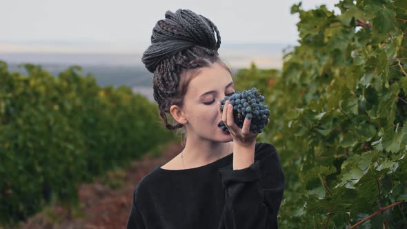 Young Woman with Dreadlocks Holding Black Grapes in Her Hands and Bites Off a Few Pieces