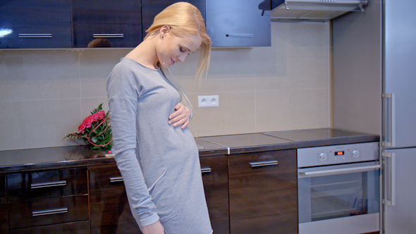 Happy Pregnant Woman Standing At The Kitchen Area