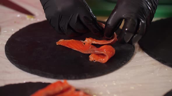 Palm Hands in Black Gloves Put Two Slices of Fat Fish on Black Stone Plate