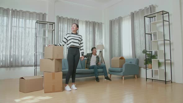 Man Sitting On Sofa To Rest While A Woman Standing And Looking Around With Stuff Into A New House