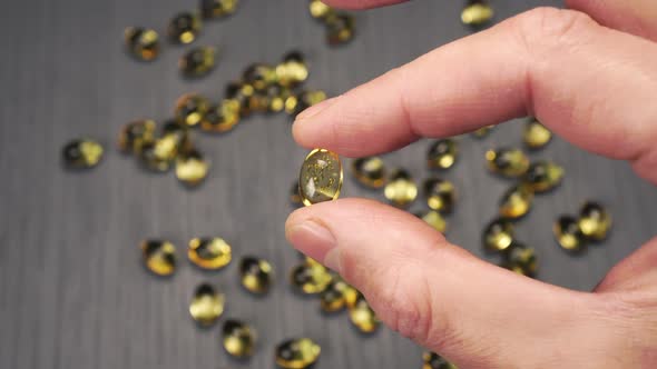 One yellow capsule of Omega 3 in hand 