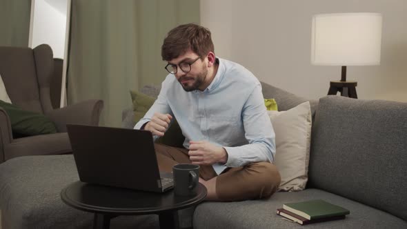 A Man in a Blue Shirt Works From Home with a Laptop