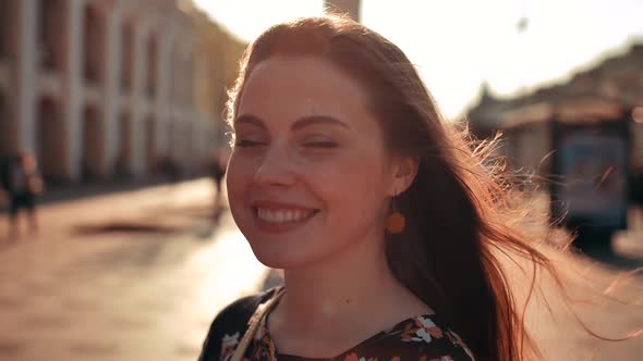 Cool Redhair with Freckles Woman in Middle of the City. Blowing Wind. Sunset Lighting