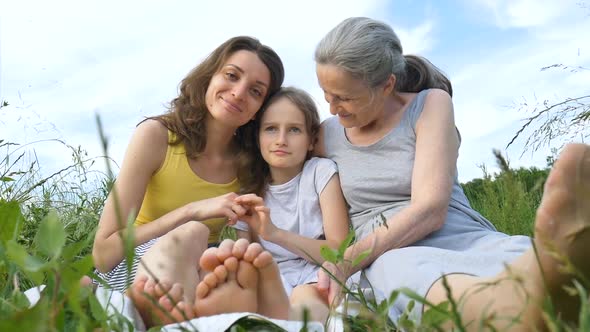 Cute Child Girl with Her Young Mother and Senior Grandmother are Having Picnic During Summer Outdoor