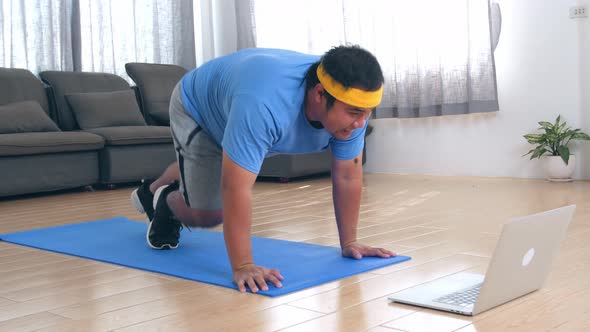 Fat Man Doing Mountain Climber Exercises While Watching Online Tutorial On Laptop