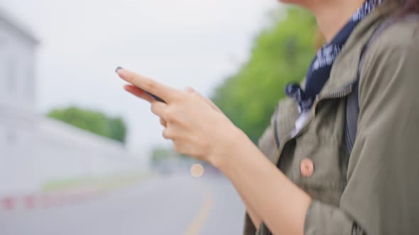 Asian woman backpacker use mobile phone chatting while walking in city.