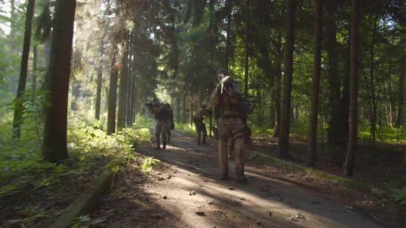 Group of Armed Soldiers Moving on Path Along Dense Forest at Daybreak