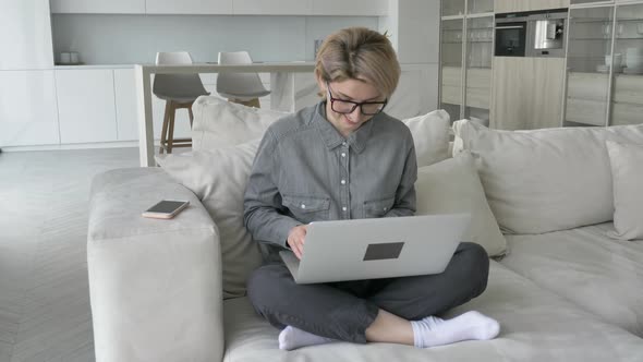 Young Woman Freelancer with Short Fair Hair Types on Laptop