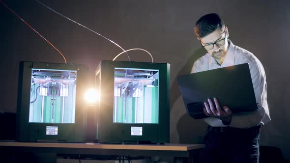 Male Engineer Is Controlling 3D-printers By His Laptop. Man Working With A 3D Printer at 3d Printing