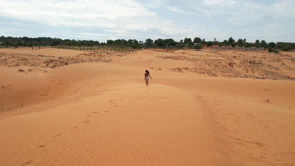 aerial tracking woman walking on top of desert dunes with footsteps in the sand in Mui Ne Vietnam