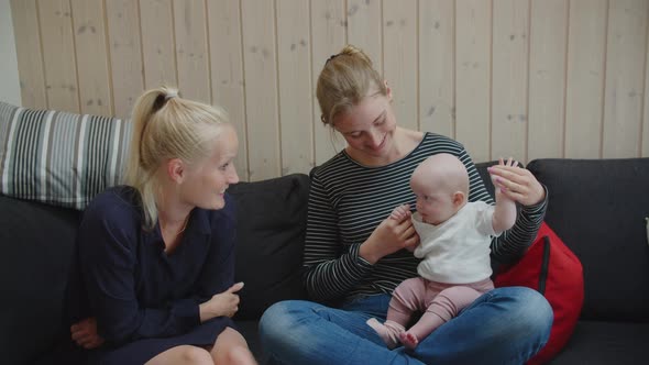 Friend Playing With Baby Girl Sitting On Mother's Lap