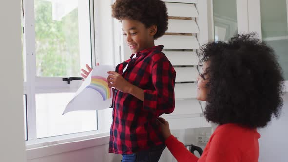 Boy sticking a rainbow painting on the window at home