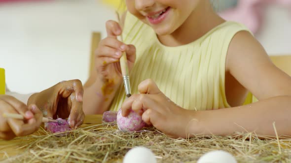 Cute Little Girl Smiling and Putting Glitter on Easter Egg alt
