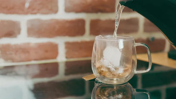Making Tea in a Bag in a Transparent Glass Cup on the Kitchen Table on a Background of Red Brick